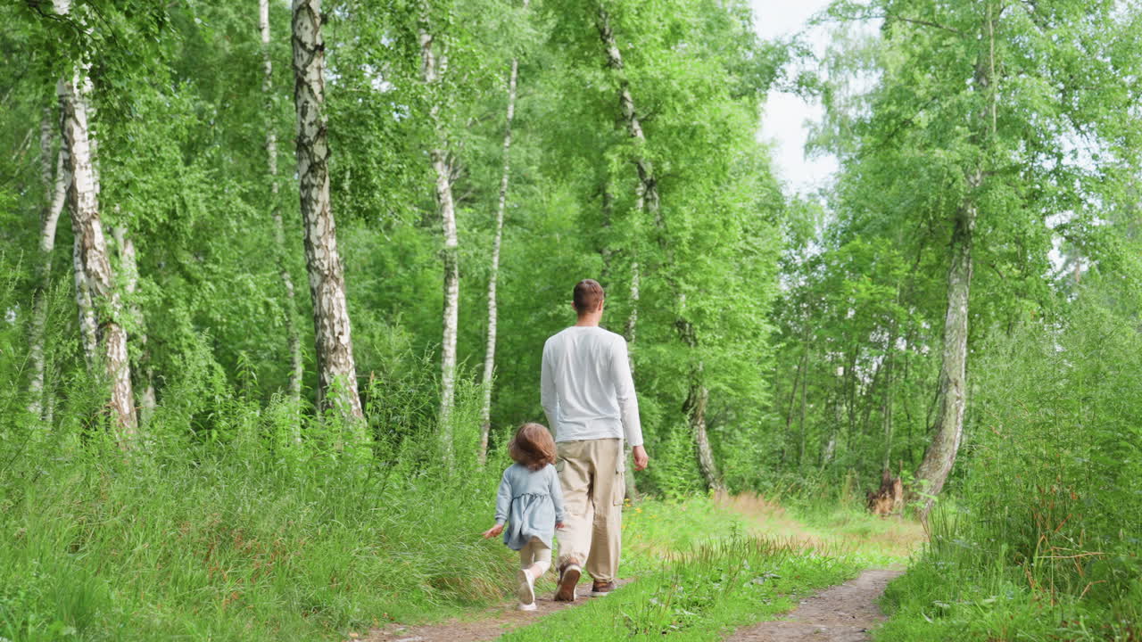 Back view of boy strolling with sister along forest path surrounded by tall birch trees and lush greenery on bright summer day, peaceful outdoor family moment in nature with warm natural light