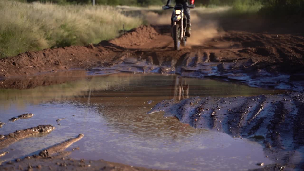 Dirt bike rider riding through a puddle of mud