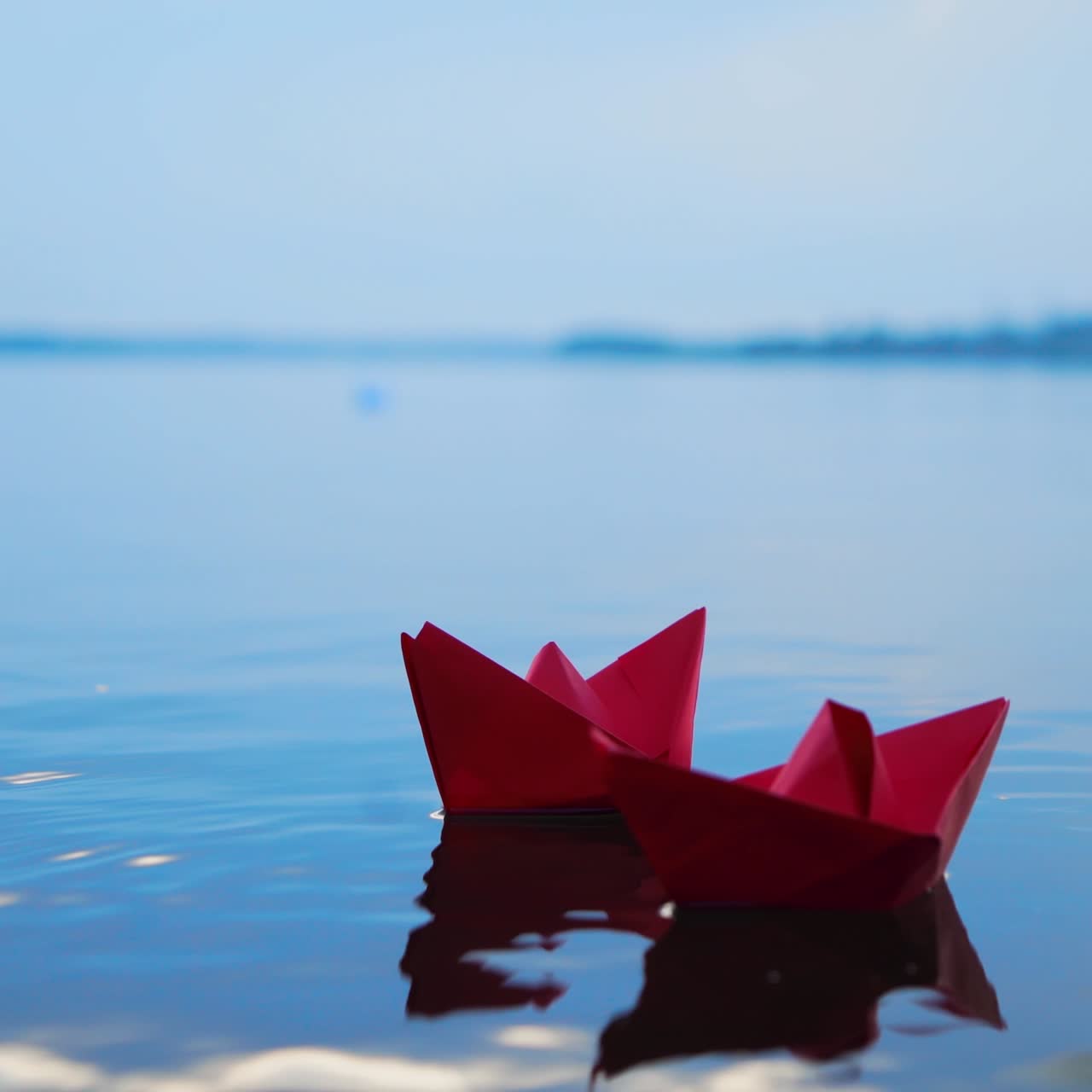 Woman's hand putting paper boat on the water. Beautiful summer sunset. Paper boat. Origami.