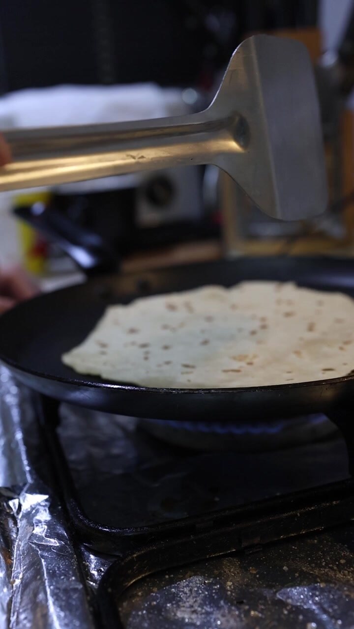 Close-up shot of a person flipping and cooking traditional flatbread on a gas stove in a kitchen