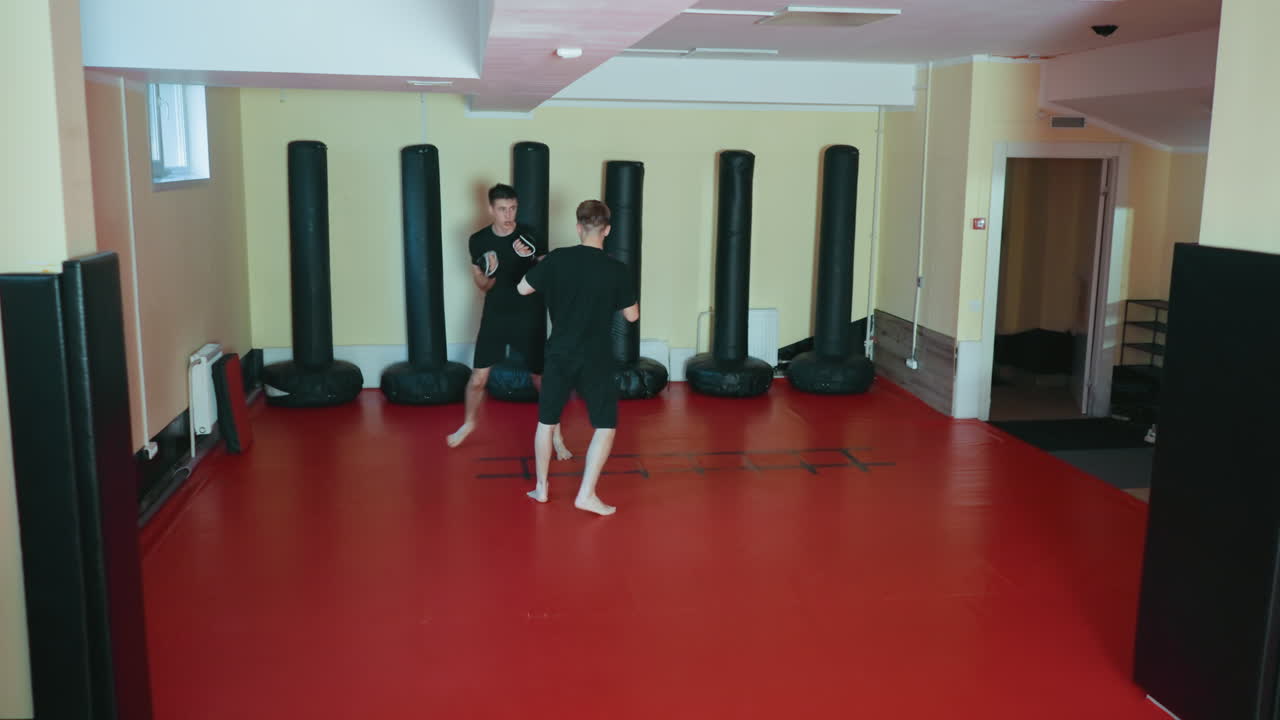 무술 체육관에서 스파링 세션을 준비하며 마주 보고 있는 운동선수들, 빨간색 매트 위에서 권투 글러브를 착용하고, 집중과 균형, 절제를 유지하며 전투 자세를 취하고, 전투 훈련을 진행하고 있어요.