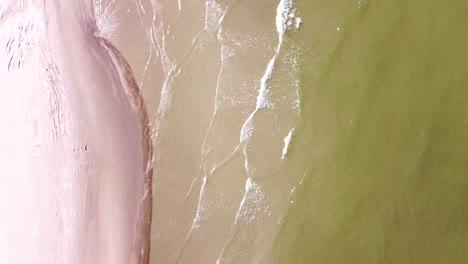 baltic sea foamy waves hitting sandy coastline in top down view