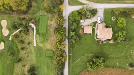 Aerial-Top-Down-View-of-Straight-Rural-Countryside-Road-and-Electric-Wire-Through-Green-Golf-Course-Field,-Neighborhood-Local-Homes-and-Lands,-Nature-Autumn-Fall-Season-Landscape