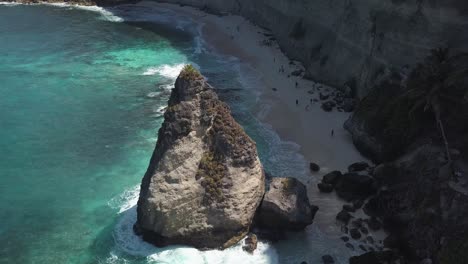 Aerial-view-of-the-crystal-blue-water-of-diamond-beach-in-Nusa-Penida,-Indonesia-with-a-prominent-large-cliff-in-the-foreground