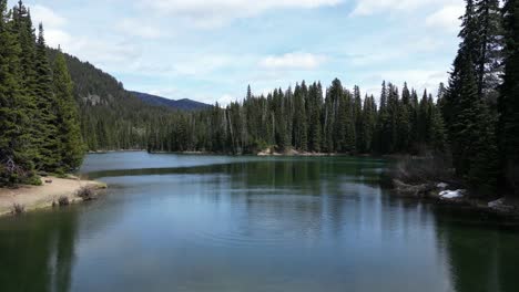 Picturesque-Lake-surrounded-by-trees-and-mountains-on-a-cloudy-day