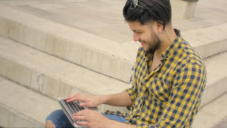 Handsome-man-siting-on-stairs-using-laptop-outdoors