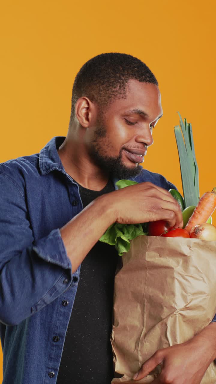 Hombre sonriente sosteniendo una bolsa de la compra con productos frescos y ofreciendo un tomate
