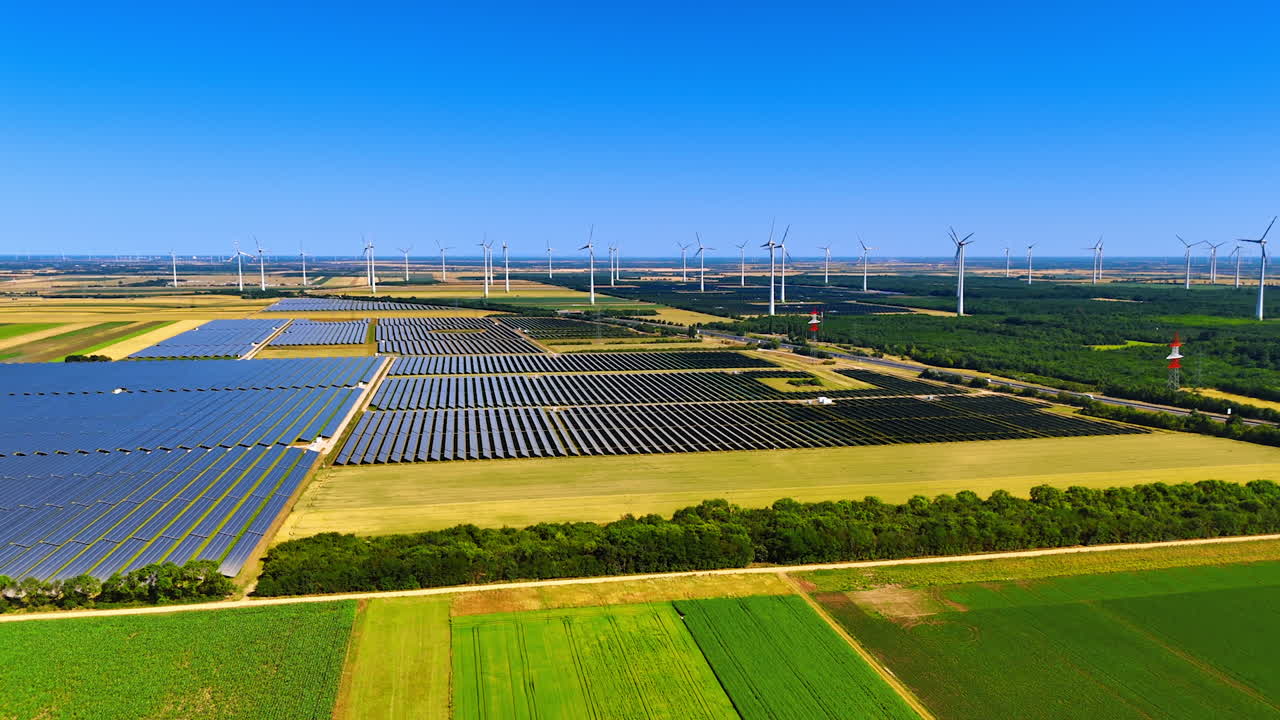 Multiple solar panels set in the countryside. Wind farms located nearby. Sustainable energy concept