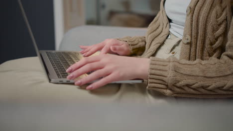 Nahaufnahme-Einer-Nicht-Erkennbaren-Frau,-Die-Auf-Einem-Laptop-Computer-Tippt,-Während-Sie-Zu-Hause-Auf-Der-Couch-Sitzt