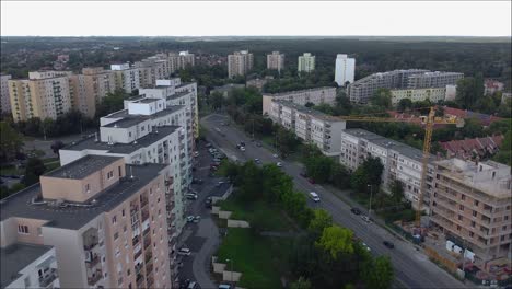 Drone-flying-over-a-town-with-traffic,-with-a-crane-in-the-frame