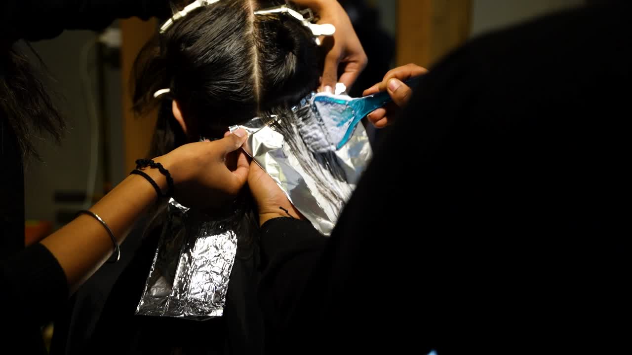 Hair stylist applying foil sheets during hair coloring treatment in salon