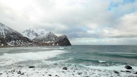 Aerial-view-of-ocean-waves-snow-covered-mountains,-Lofoten-Islands,-Norway