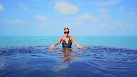 feliz mujer asiática rociando agua en una piscina infinita en un día tropical soleado