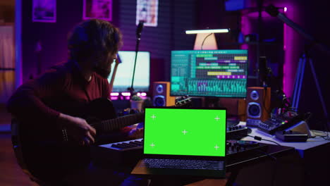 Guitarist-playing-his-acoustic-instrument-next-to-greenscreen-on-laptop