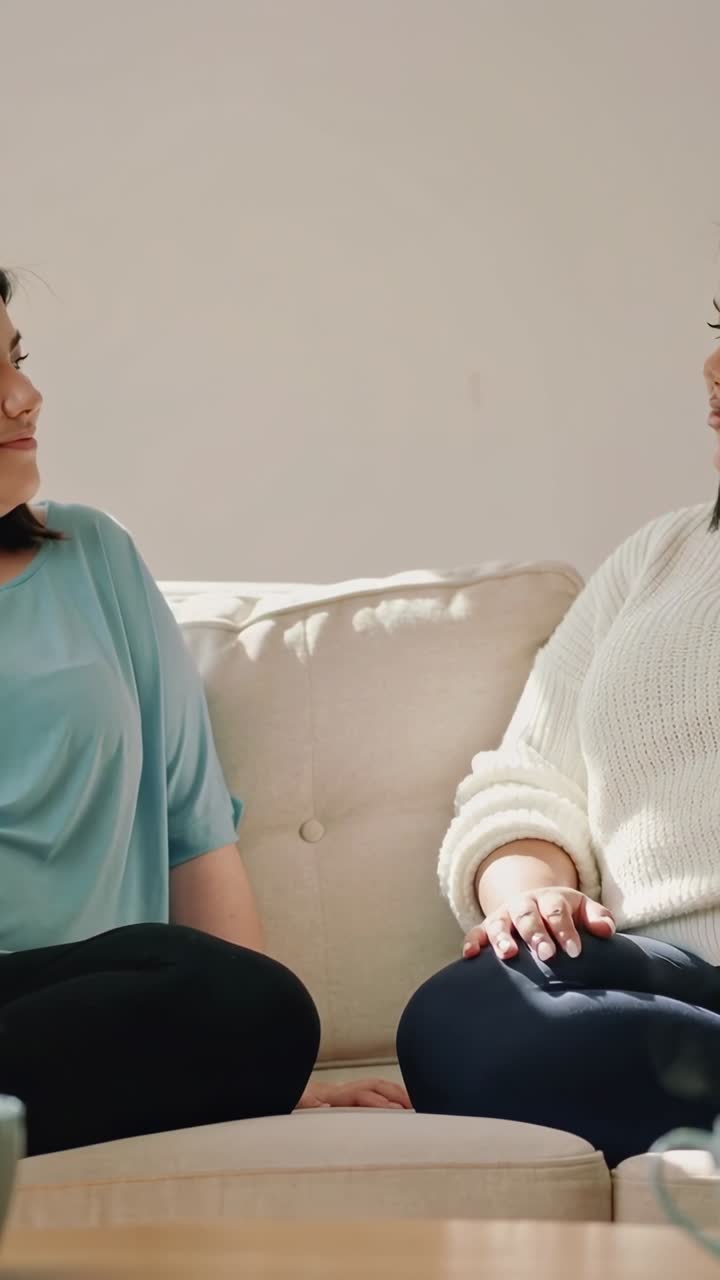 Vertikal video: Taler i sofa derhjemme, kvinde i hvid sweater gestikulerer og understreger pointe med krus.