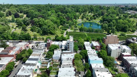 Aerial-trucking-shot-of-idyllic-lake-in-park-and-residential-area-of-Brooklyn-during-sunny-day-in-New-York-City