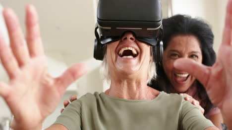 Happy-diverse-senior-women-using-vr-glasses-and-laughing-in-sunny-living-room,-slow-motion