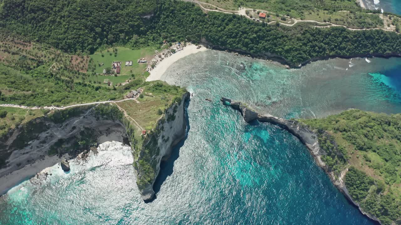 A striking drone aerial shot of the East Nusa Penida coastline, highlighting the distinct coves of Diamond Beach and Atuh Beach (known for its iconic arch-shaped rock formation in the water)