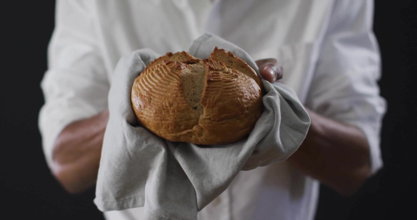 Baker Holding Freshly Baked Artisan Loaf of Bread