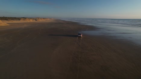 Drohne-Folgt-Dem-Auto,-Das-Bei-Sonnenuntergang-Am-Langen-Sandstrand-Fährt