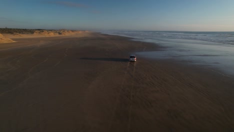 drone follow car driving on long sandy beach during sunset