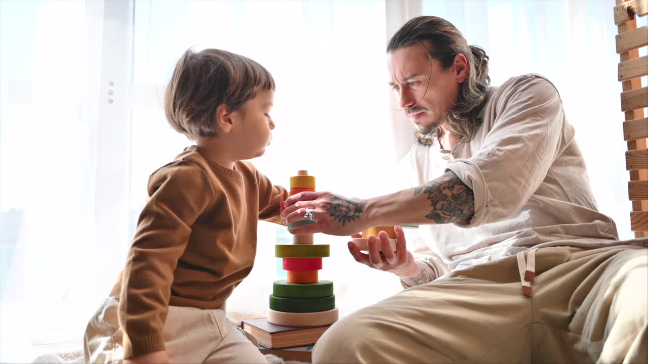 Father playing with his son with colourful, ecological wooden toys near a window