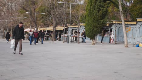 Cuesta de Moyano iconic pedestrian street in Madrid which holds a permanent book fair. Row of book stalls with blue fronts and yellow awning. Winter morning. Locals having a walk. Spanish lifestyle.