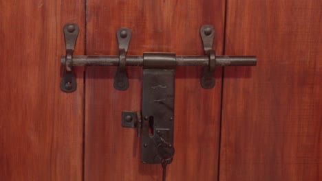 Close-up-of-a-vintage-metal-latch-securing-a-wooden-door,-highlighting-its-rustic-and-sturdy-design