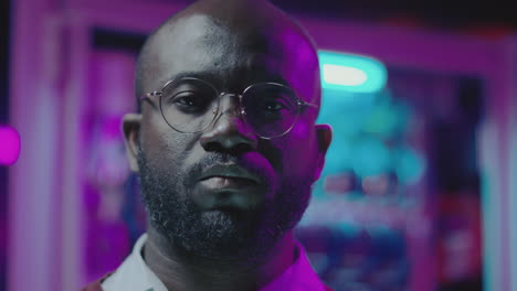 close-up portrait of a man with glasses and beard under neon lights