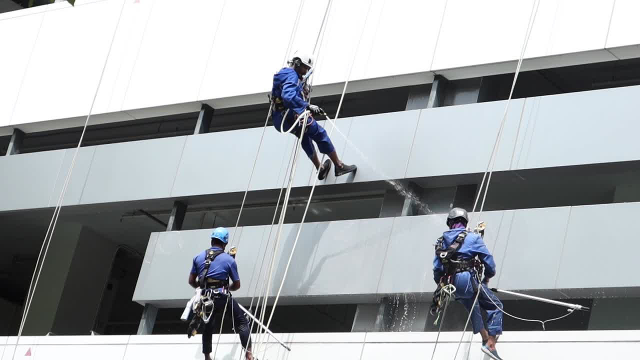 tres trabajadores limpiando un edificio de gran altura usando acceso por cuerda