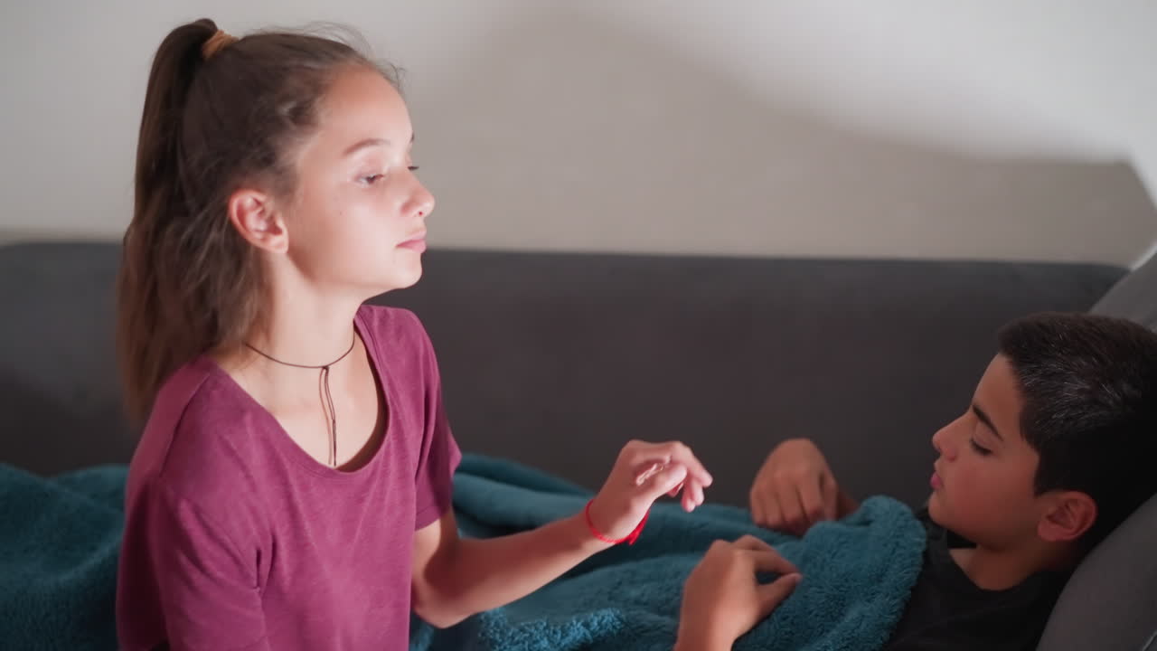 young boy faking sleep as sister finishes covering him with blanket, turns to look at her as she leaves, playful sibling moment, thoughtful care, family bonding, sibling love, quiet care gesture