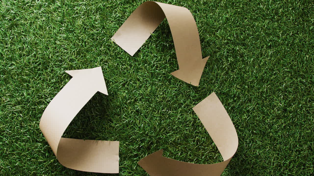 primer plano del símbolo de reciclaje de flechas de papel sobre fondo de hierba, con espacio para copiar