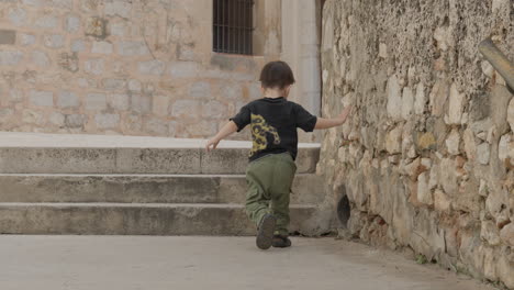 little boy having fun exploring old stone rubble stairs and a hole in the wall, points at it and climbs up