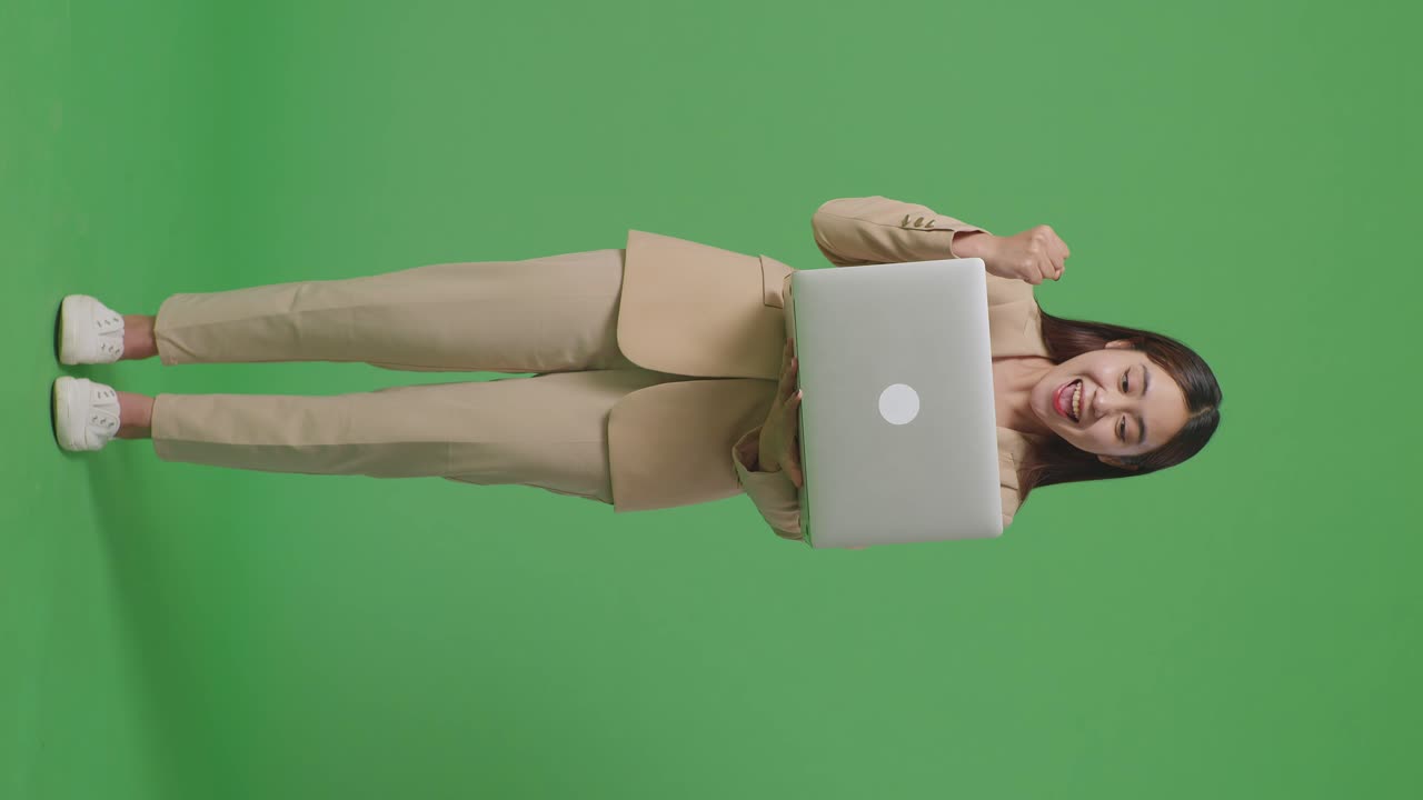 cuerpo lleno de feliz mujer de negocios asiática celebrando usando computadora portátil en pantalla verde en el estudio