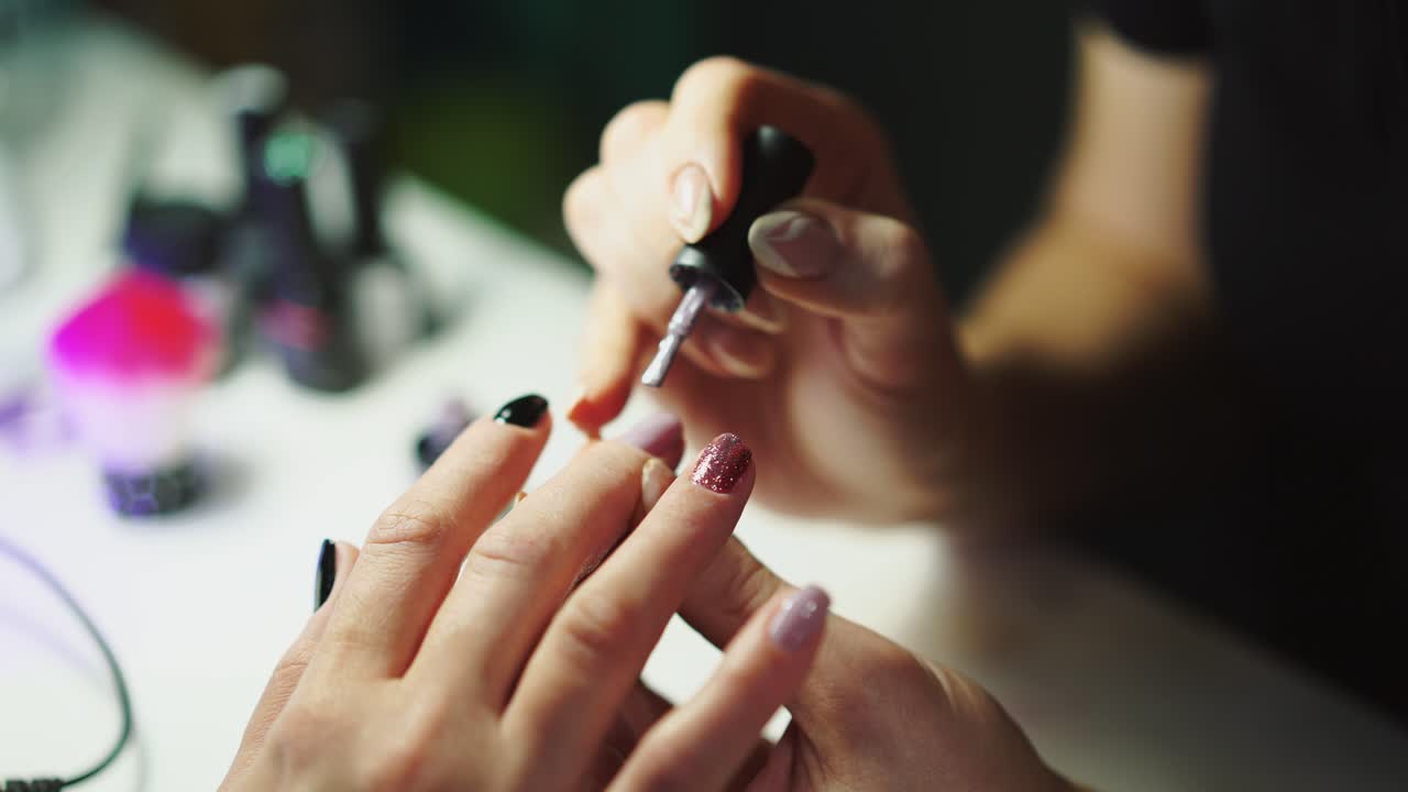 master is making a manicure by gel-lacquer in black and pink colours for client in tha salon of beauty