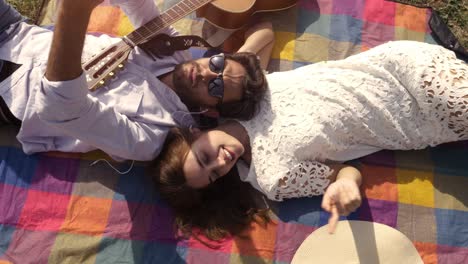 happy lovely young couple lying on colorful blanket in the park taking selfies smartphone romantic with guitar sunglasses beautiful attractive girl top view rotating camera slow motion