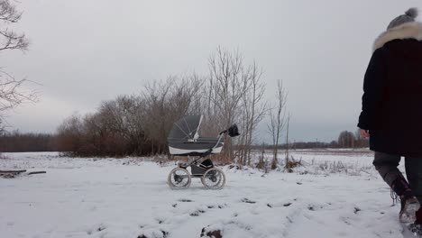 carruaje de bebé en un camino de campo nevado, la madre camina y continúa la actividad