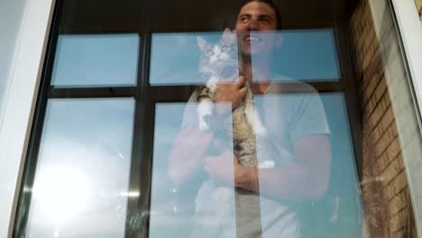 joven feliz sostiene un gato en sus manos y va a la ventana para mirar a la calle. amor por las mascotas.