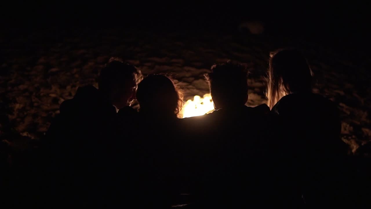 늦은 밤에 불  ⁇ 에 앉아서 서로 포옹하는 젊은이들의 뒷모습. 즐거운 친구들이 이야기하고