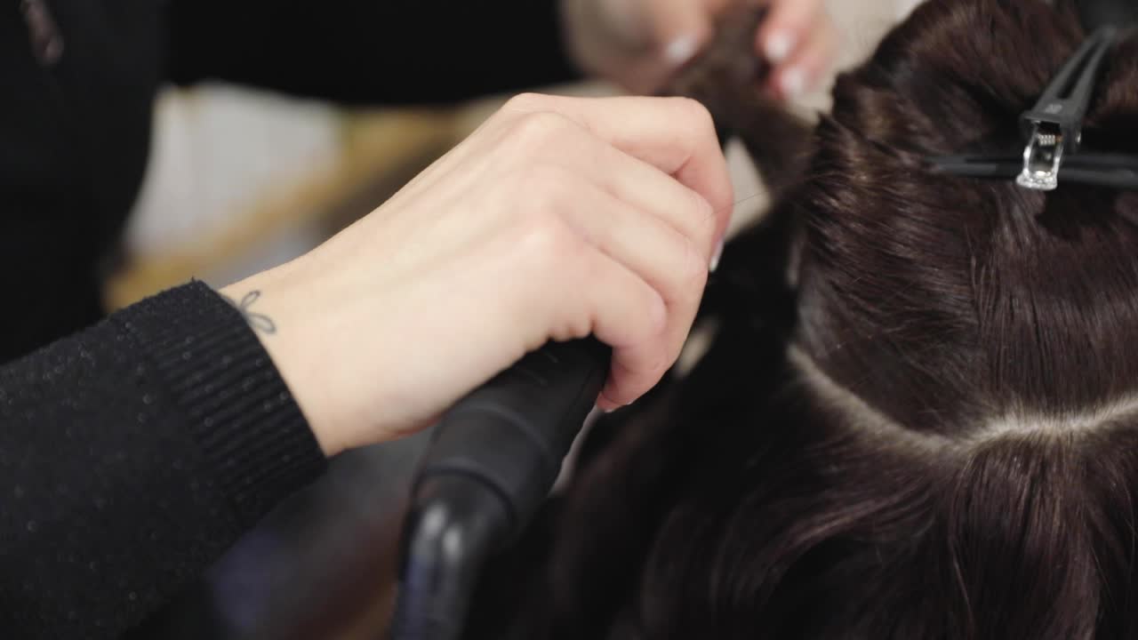 Hairdresser doing female hairstyle with hot tongs in barbershop. Beauty and style concept.