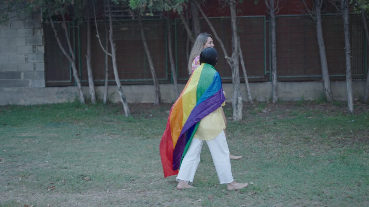 Two Women Walking with a Rainbow Pride Flag in a Park