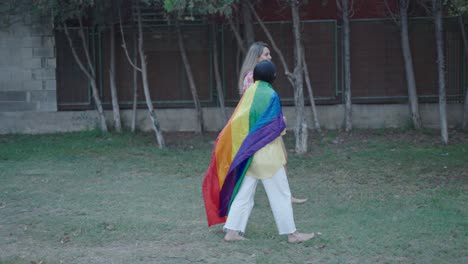two women walking with a rainbow pride flag in a park