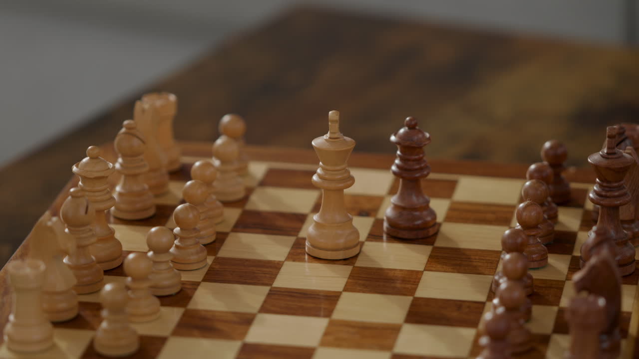 A hand reaches for the king piece on a wooden chess board. The game is ongoing with pieces arranged and a player contemplating the next move. It is a familiar setting for strategy