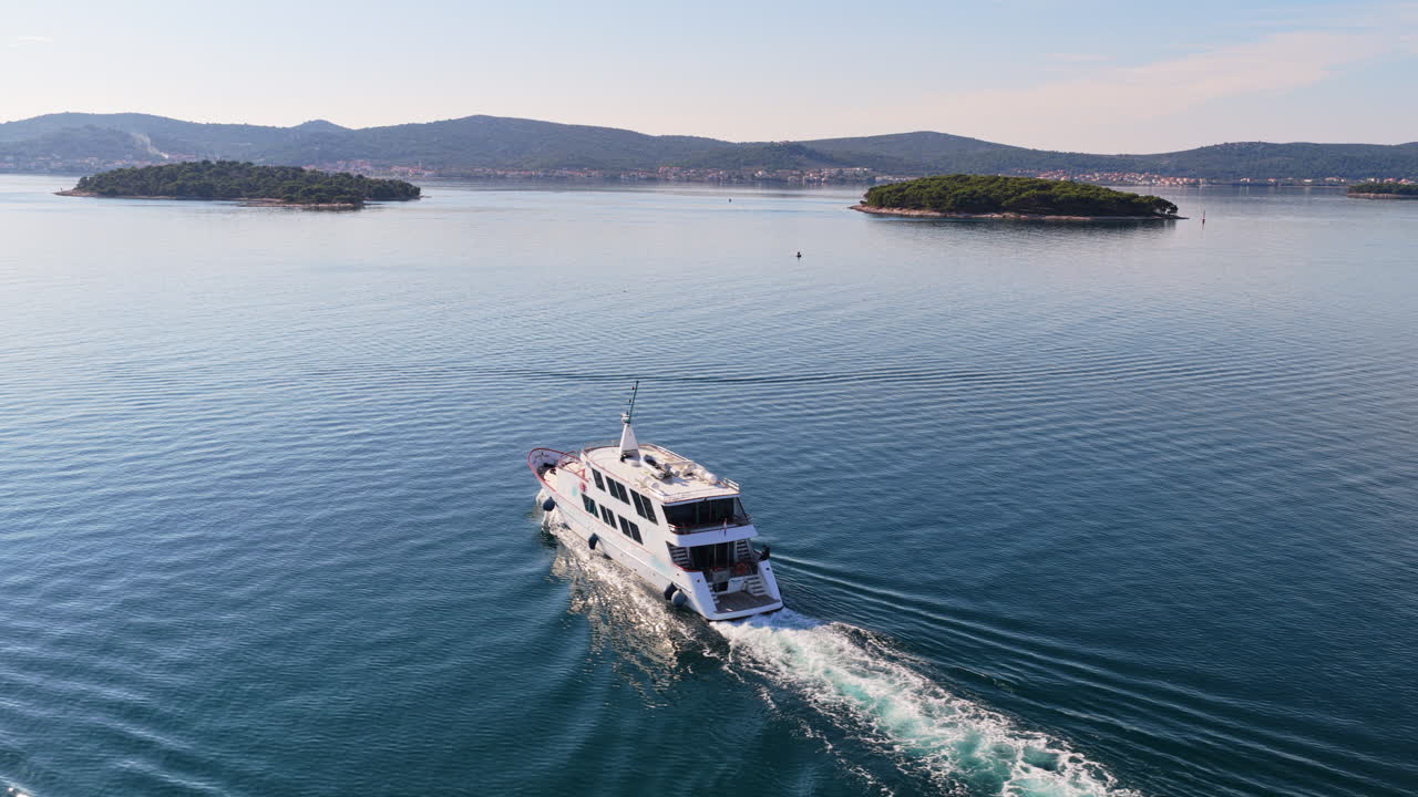 Vista aerea da drone di un yacht bianco che naviga in acque blu calme, incorniciato da isole e colline alberate. Biograd na Moru, Croazia