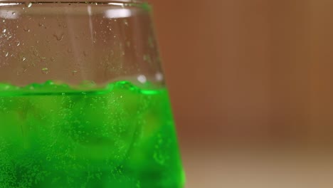 close-up of a bright green beverage with ice cubes in a transparent glass against a blurred background.