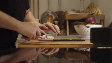 chef sharpens knife on the sharping stone on the kitchen table