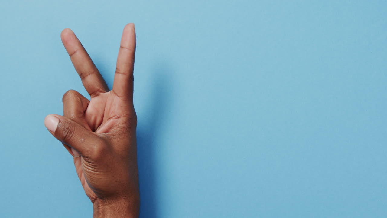 cerca de la mano de un hombre biracial que muestra un signo de paz con espacio de copia en un fondo azul
