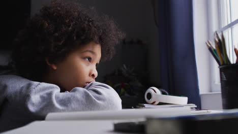 mixed race girl sitting by desk looking through window