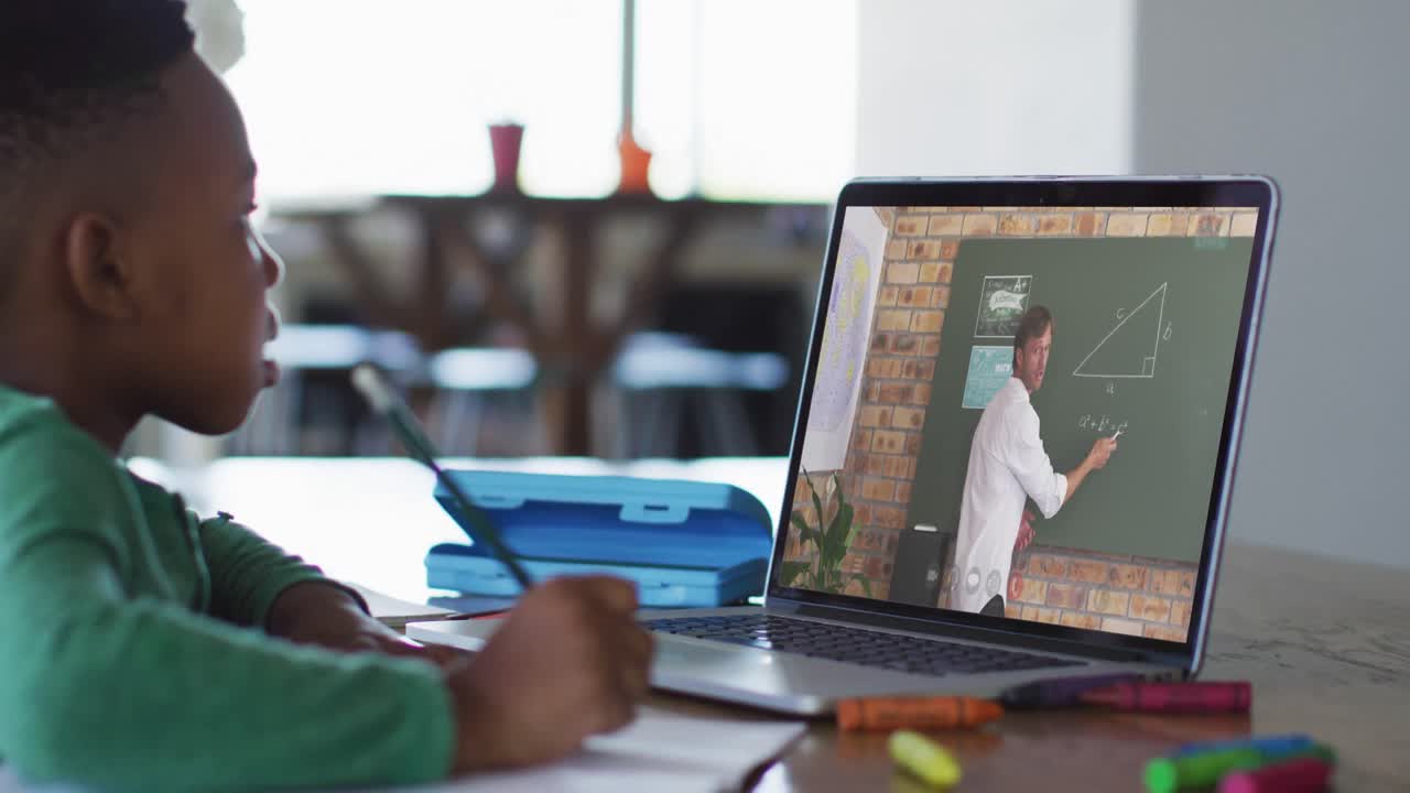 niño afroamericano haciendo la tarea mientras tiene una videollamada con un profesor masculino en una computadora portátil en casa
