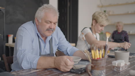 A-group-of-elderly-people-at-a-master-class-in-pottery-together-sculpt-and-cut-a-drawing-on-cups-of-clay-for-the-manufacture-of-ceramic-dishes